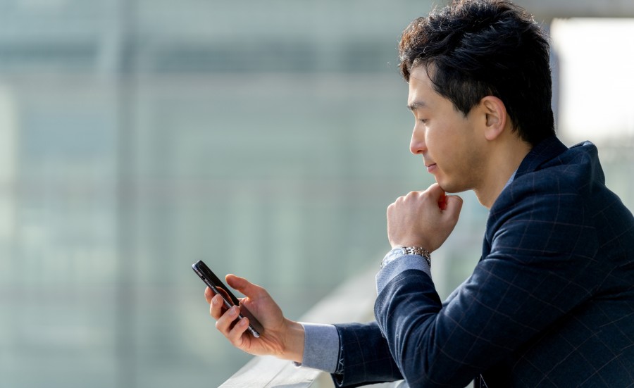 スマートフォンの画面を見て悩む男性