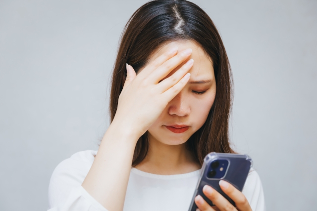 スマホを見ながら頭を抱える女性